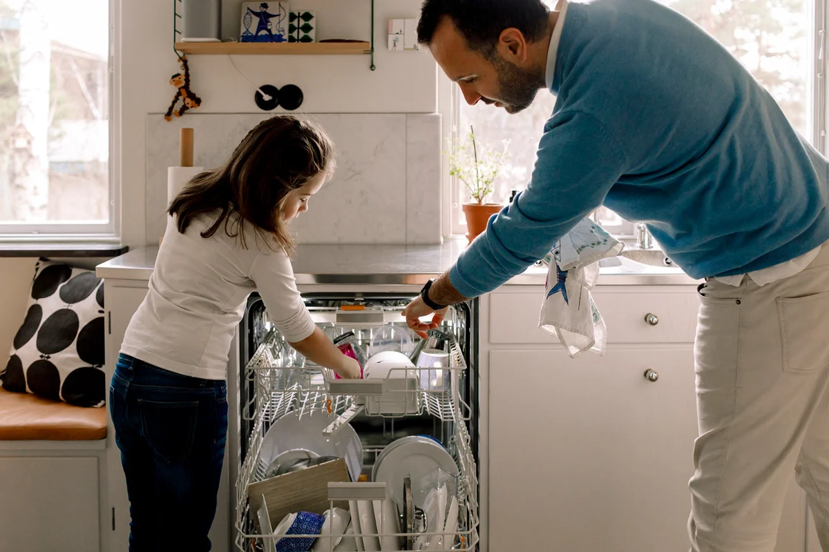 Father and daughter arranging utensils in dishwasher at kitchen