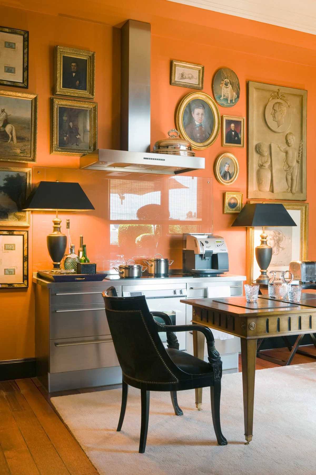 'Hermes' orange walls and closely grouped pictures in kitchen with Gaggenau appliances