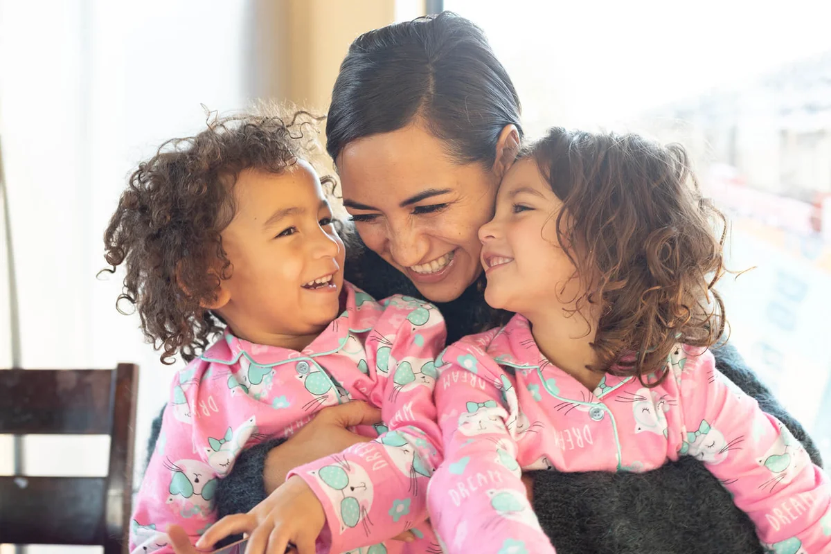 Happy embrace between mother and twin daughters in pyjamas