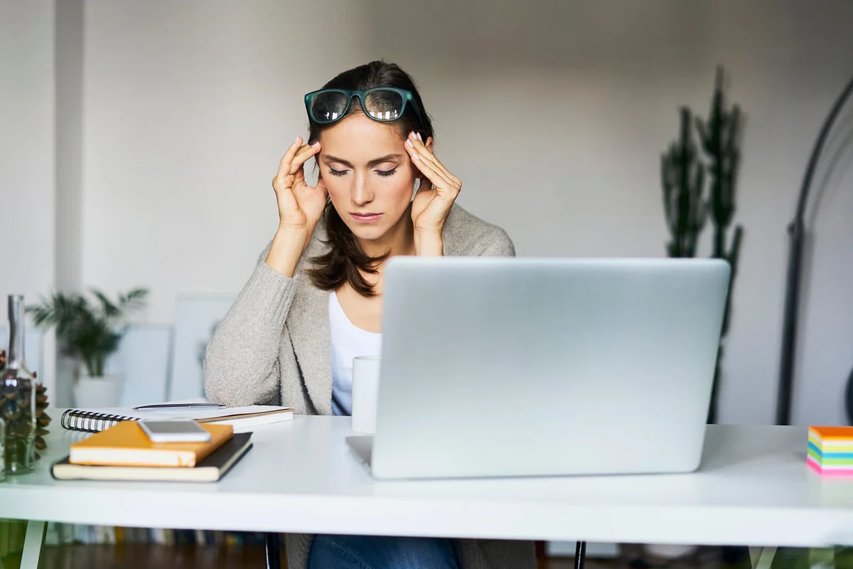 woman at home with laptop on desk touching her temples