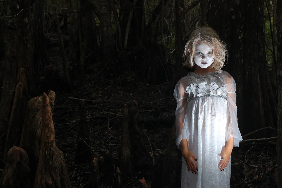 A 7 year old little girl dressed up as a Ghoul or Ghost inside of a dark creepy cypress swamp, surrounded by huge cypress root