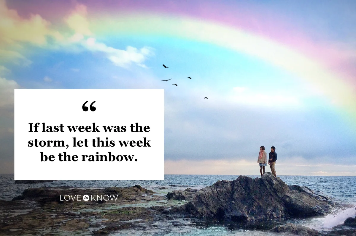 Man And Woman Standing On Top Of Rock Amidst Sea Looking At Rainbow