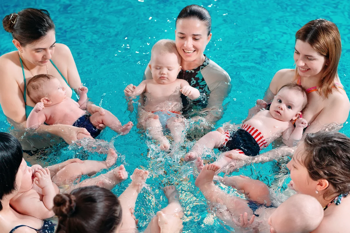 A group of mothers with their young children in a children's swimming class