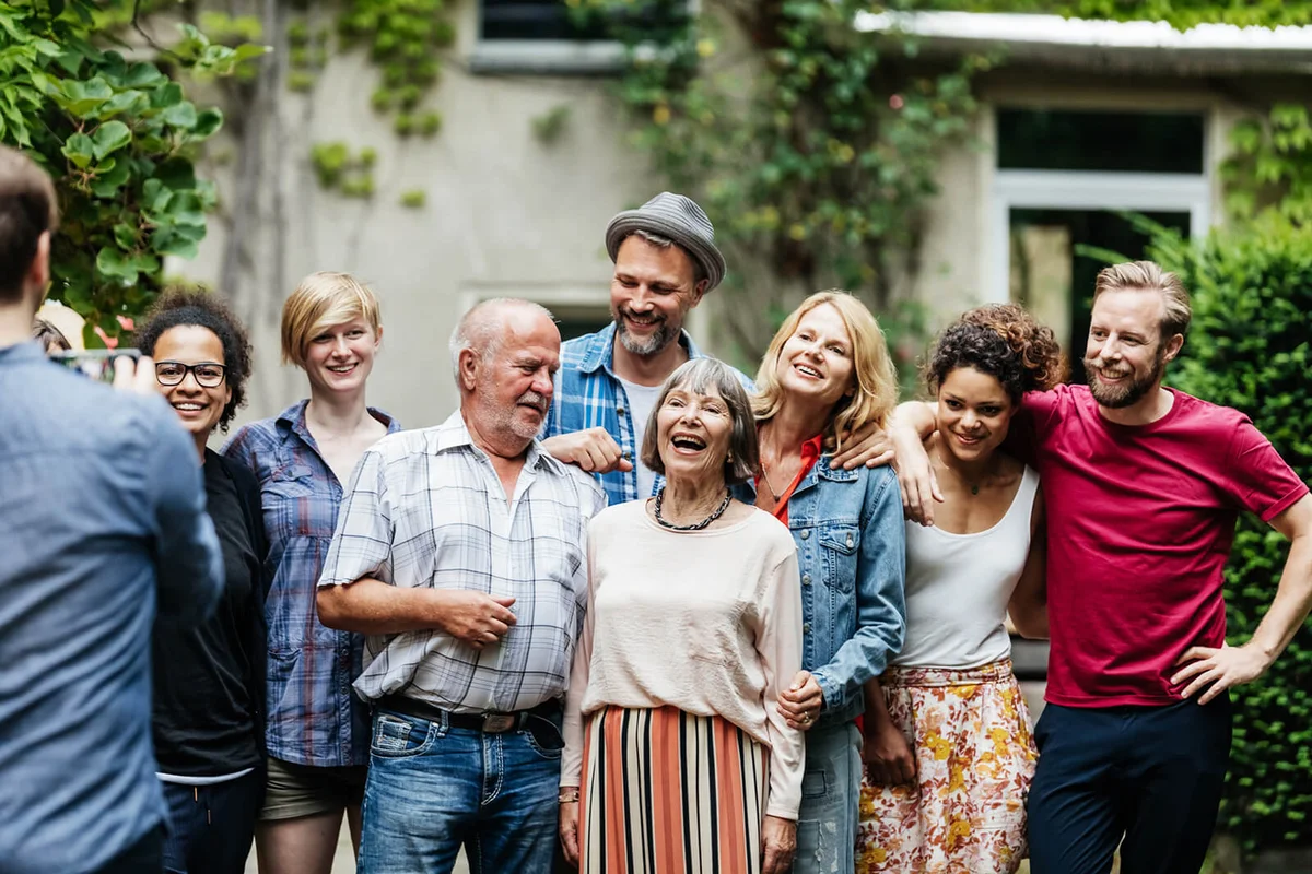 A man taking a group photo with his family and friends as a barbecue in a courtyard
