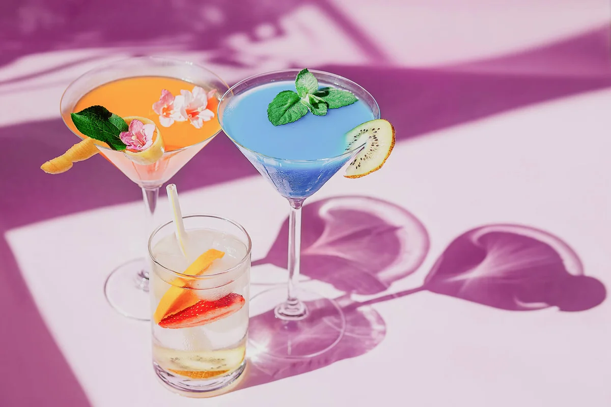 Sparkling glasses of cocktails and sliced fruit on a pink table background