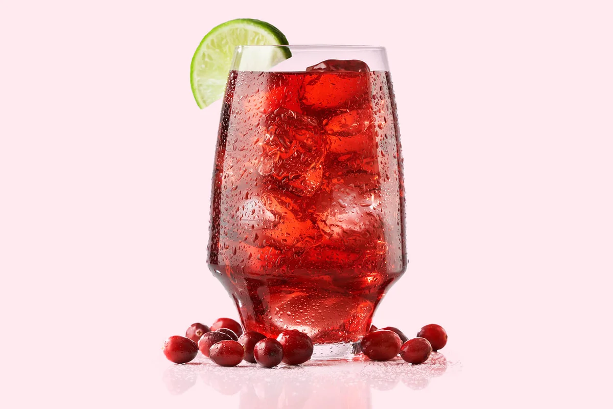 A wide tall glass of fresh cranberry juices served with lime