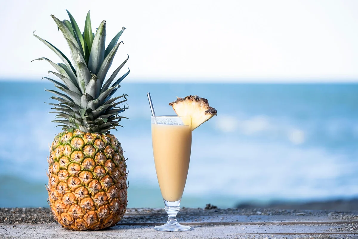 pineapple juice in a glass glass next to the beach