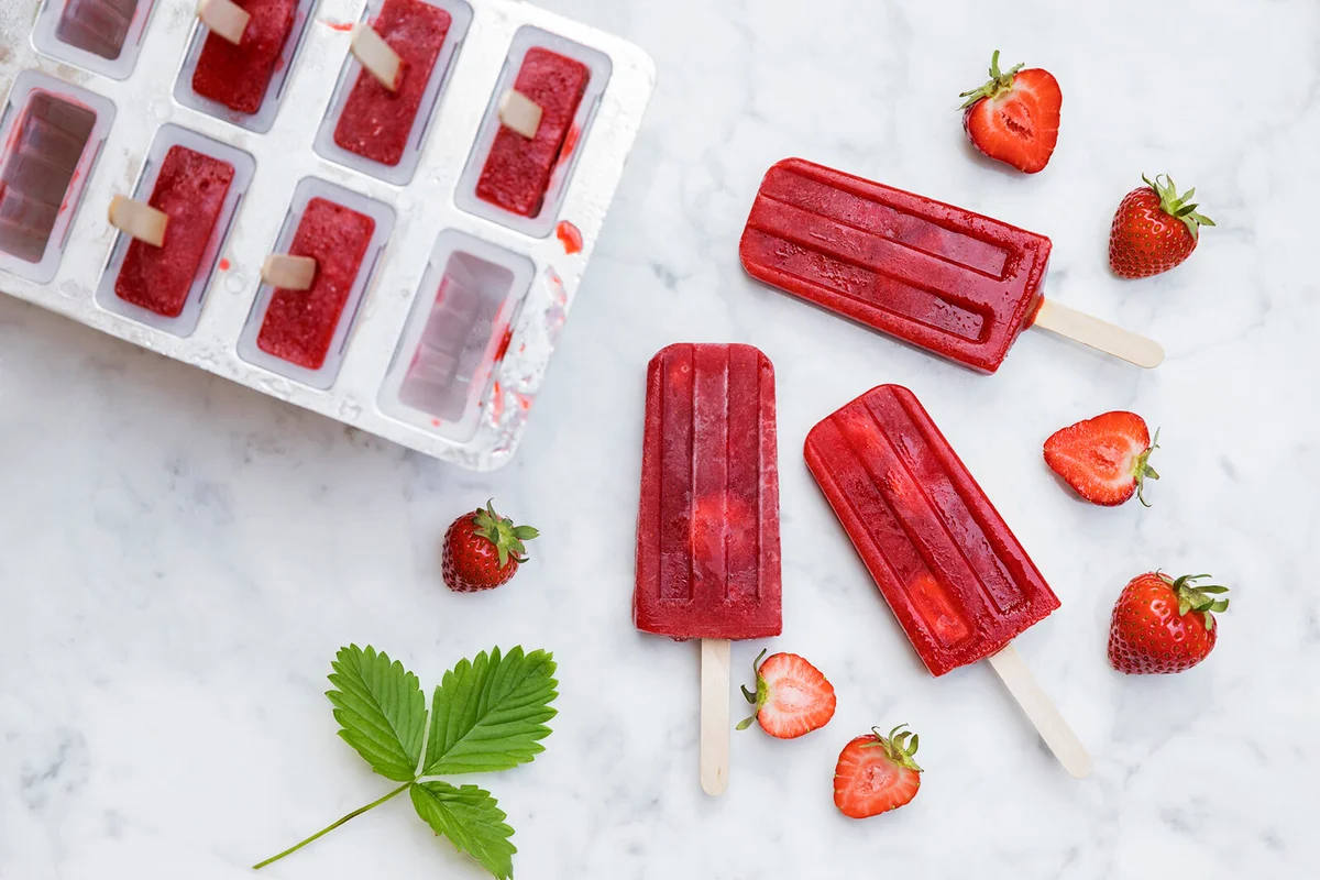 Homemade strawberry popsicles lying on marble surface