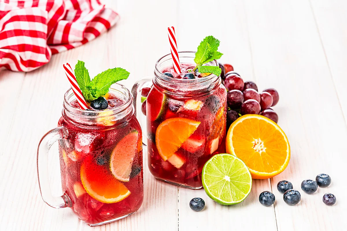 Two Mason jars of cold refreshing sangria with fruits on white table