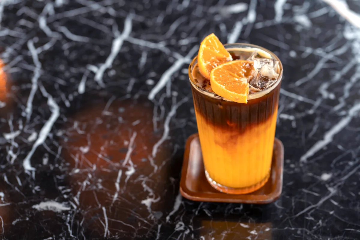 Black sambuca mixed with orange juice with orange slices on the glass