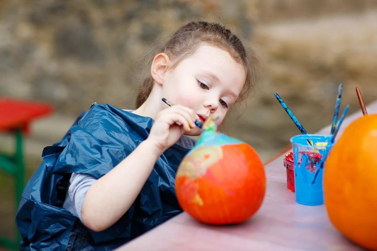 Little kid girl painting with colors on pumpkin