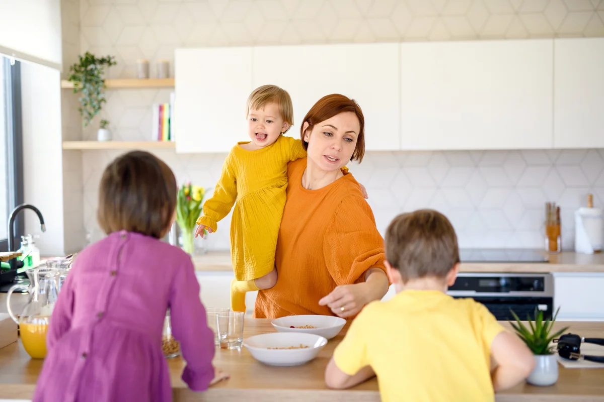 Mother with three small children indoors in kitchen in the morning at home