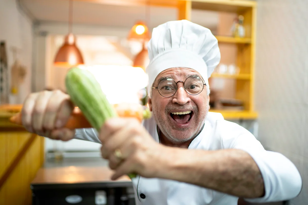 Man dresses as chef while holding a cucumber and a carrot