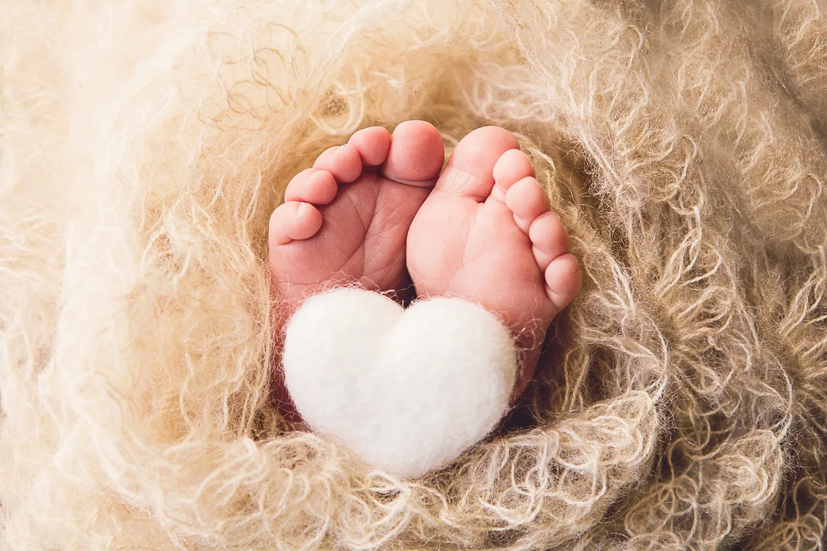 A close up image of a newborn's tiny feet, with a small, felted heart