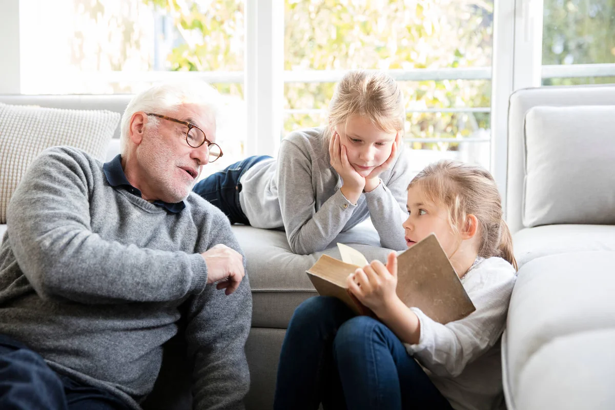 Two girls and grandfather reading book in living room