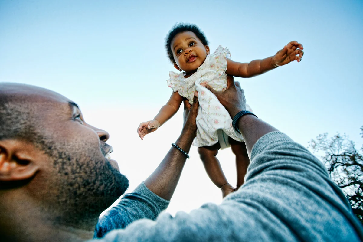 father holding baby daughter under blue sky