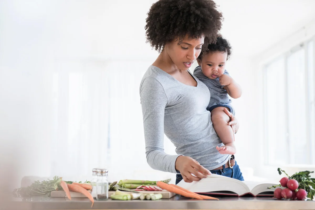 Mother reading cookbook while holding baby son
