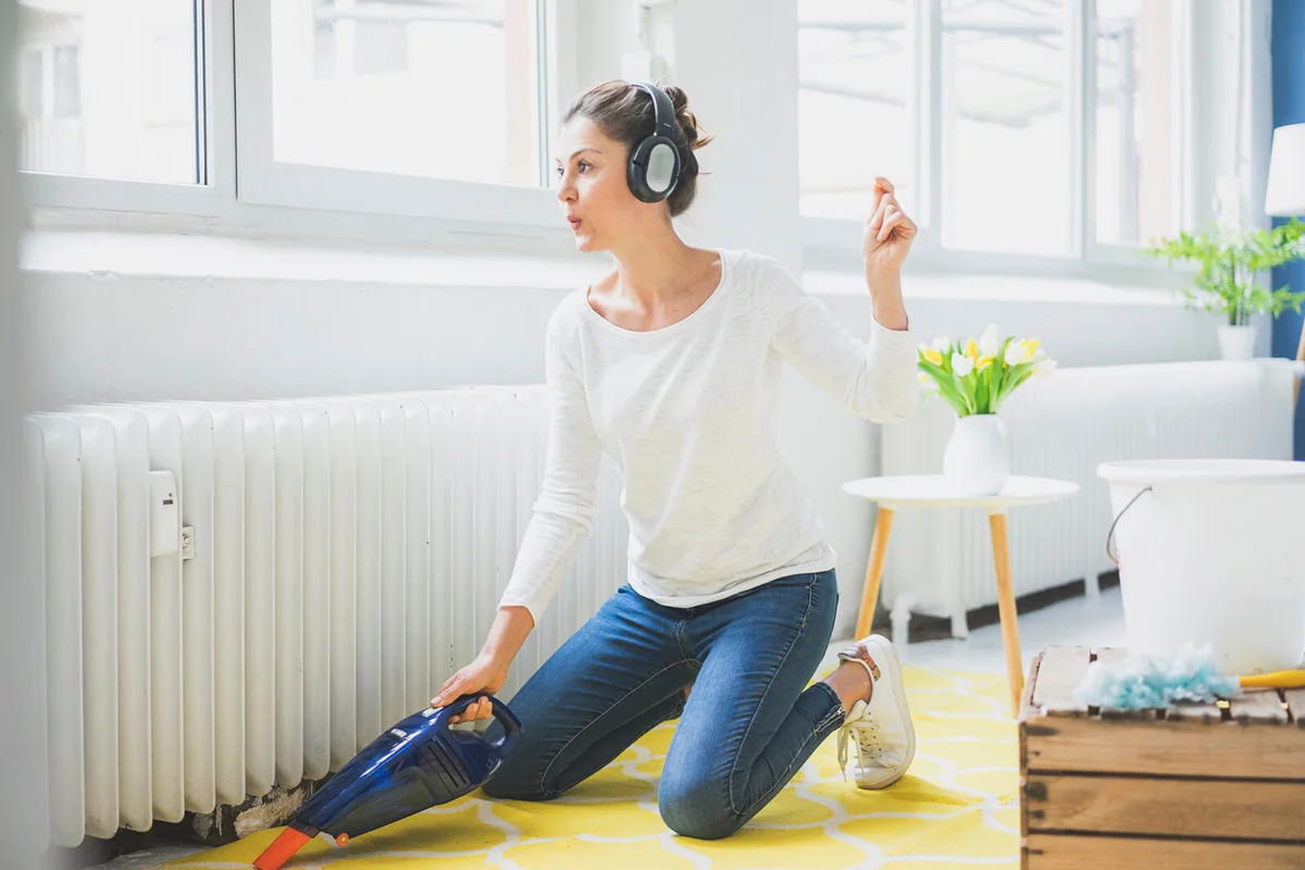 Woman at home wearing headphones hoovering the floor