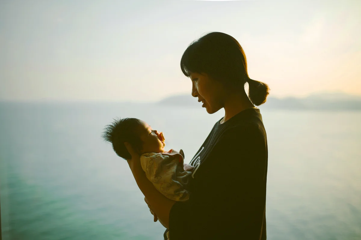 Mother hugging baby girl at home in front of window