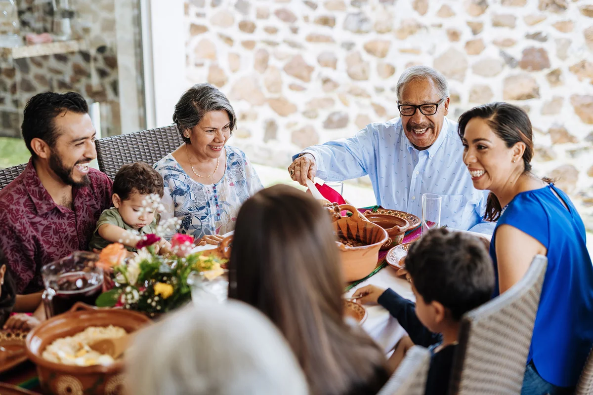 Latin senior man serving the food to his family at dinner table