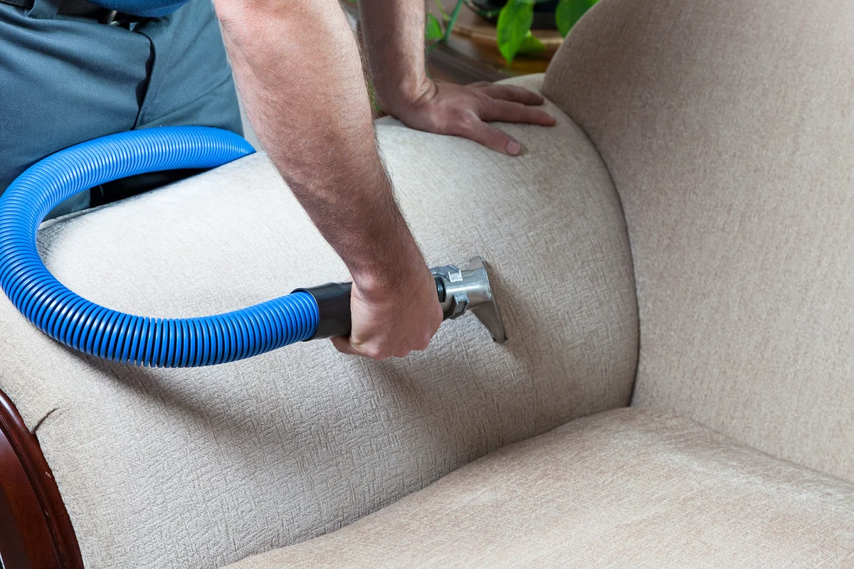 Man cleaning sofa with steam cleaning in home