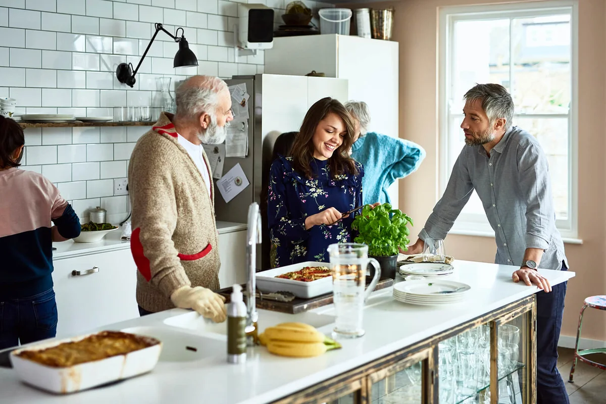 Woman cutting fresh basil with husband and father in law in family kitchen