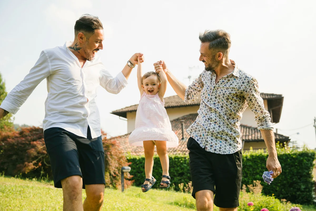 Happy gay couple playing with their child in the garden