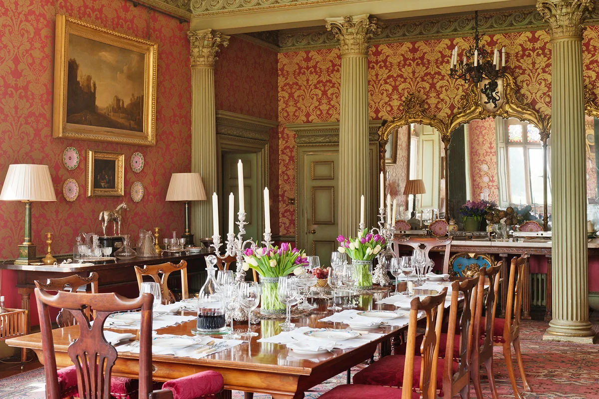 Laid table in large dining room with red and gold design wallpaper