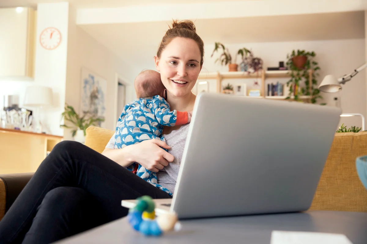 Mother using laptop and holding her newborn baby at home