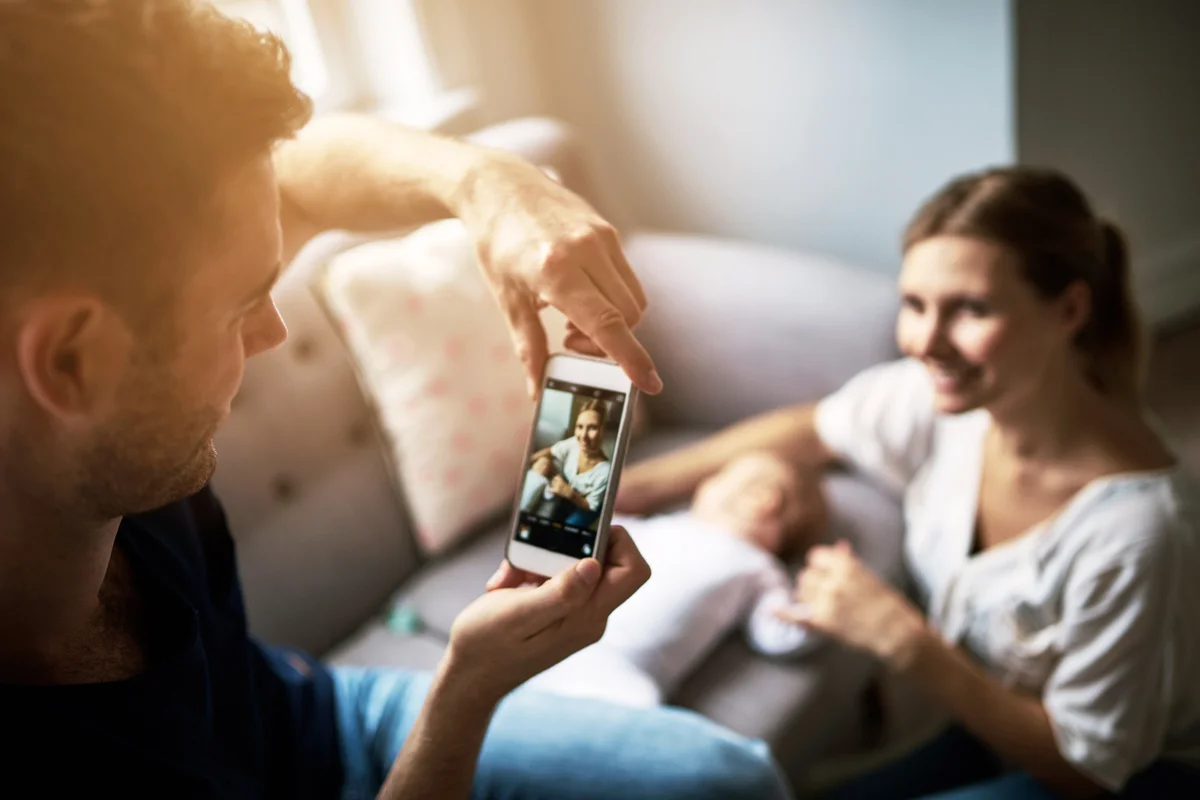 Man taking photos of his wife with their new baby on a phone at home