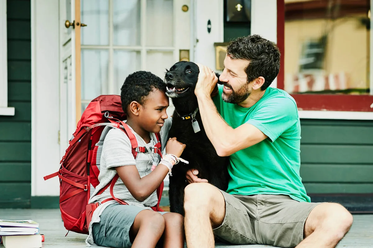 Father and son sitting on front porch of home with dog before going on backpacking trip