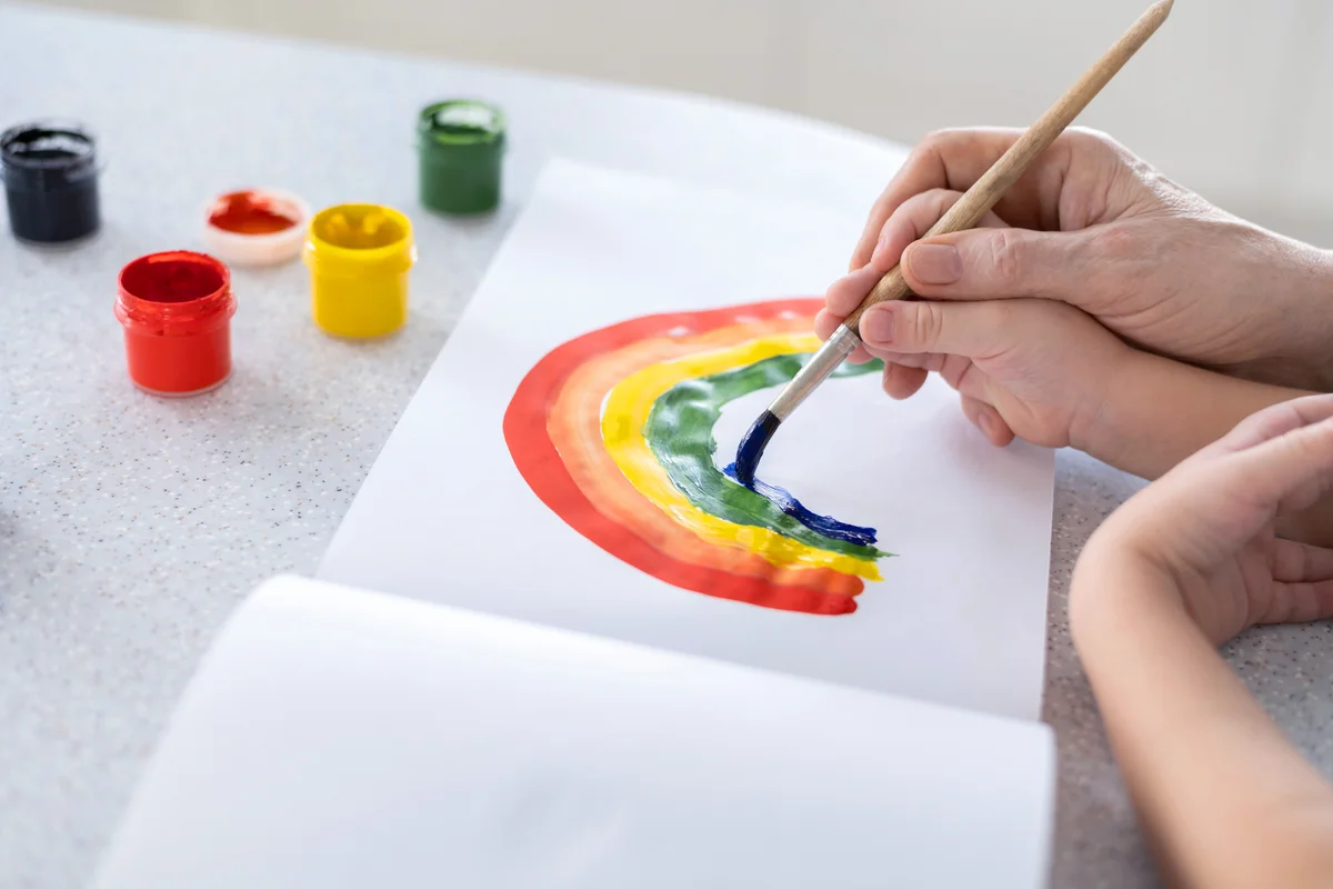 Hands of a child in the hands of an adult learn to draw a rainbow