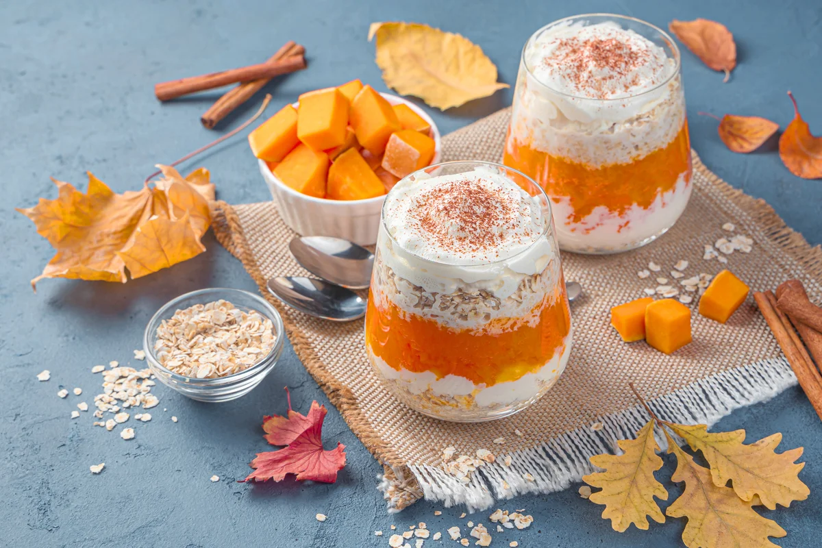 Autumn dessert with pumpkin, cereals and cream on a dark blue background with leaves
