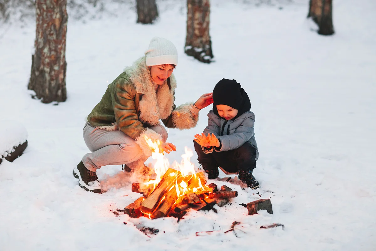 Mother And Son In Snow During Winter With Bonfire