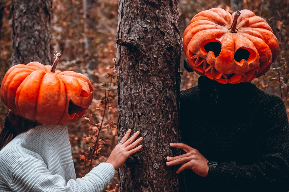couple wearing pumpkin costume hiding behind tree