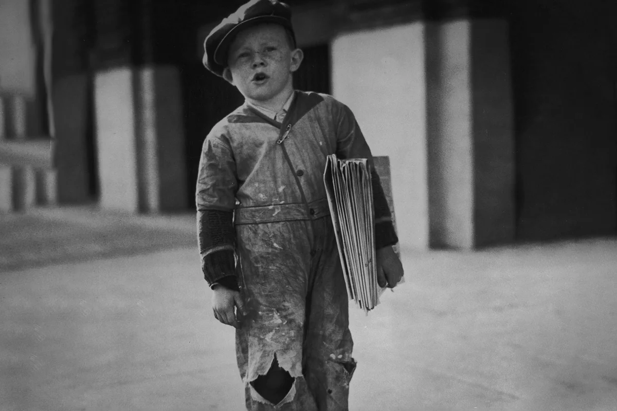 young newsboy stands on the sidewalk selling newspapers 1925