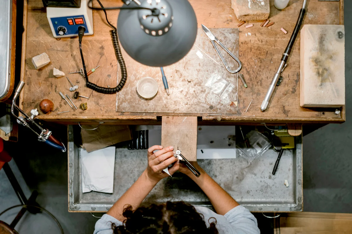 Overhead view of female jeweller using coping saw at workbench