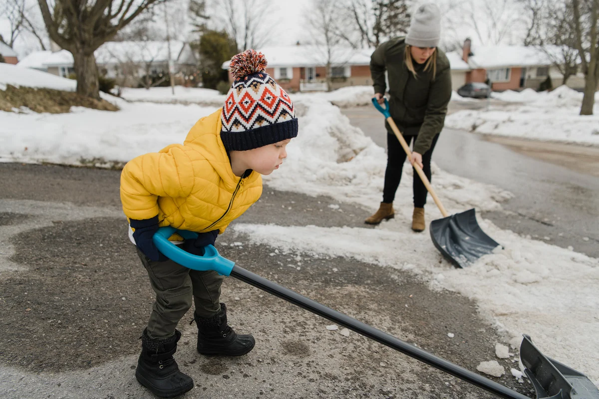 Son helping mother while shoveling snow on driveway