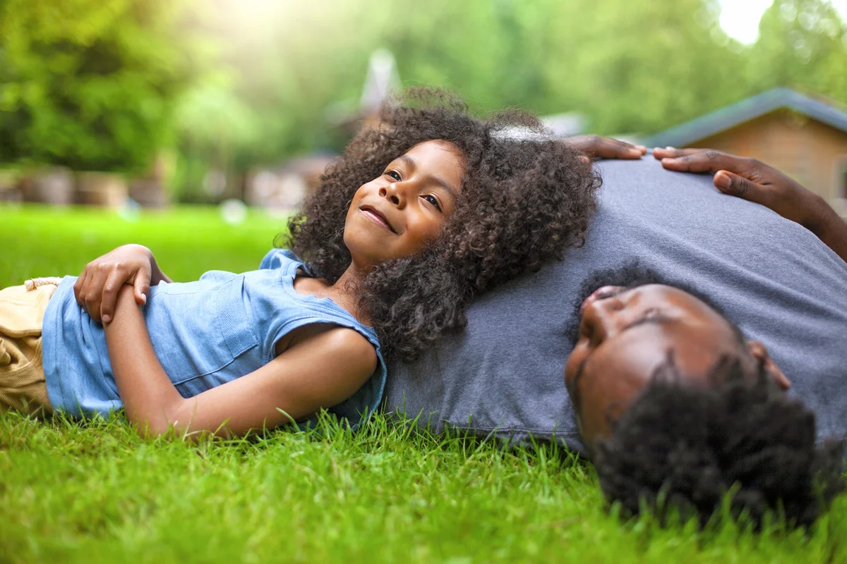 African-American son and father rests on grass