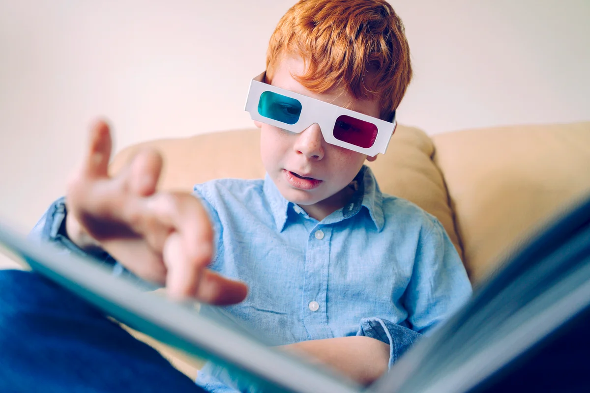 Curious little boy wearing three dimensional glasses and reading a book