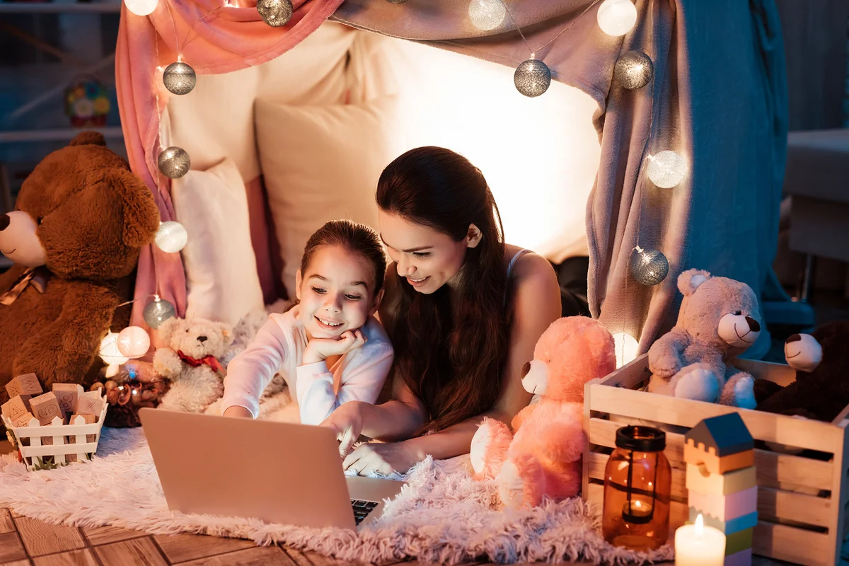 Mother and daughter watching movie on laptop in pillow house