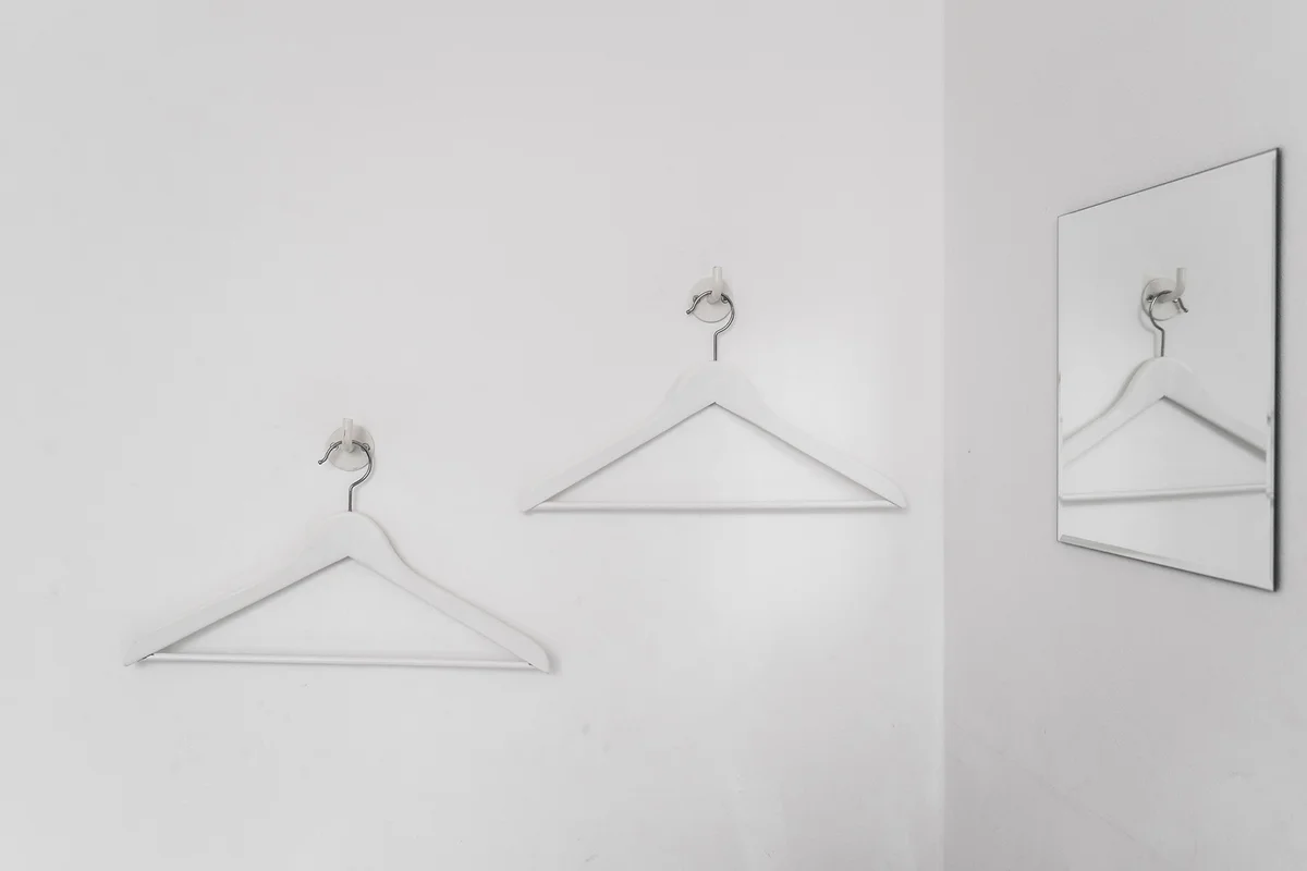 Coathangers Hanging From Hooks Mounted On White Wall