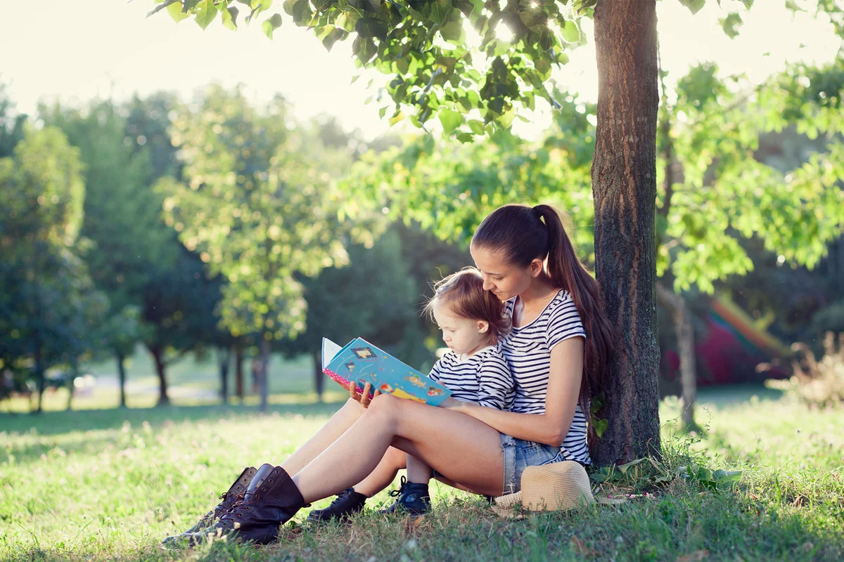 mother reading to toddler child under tree