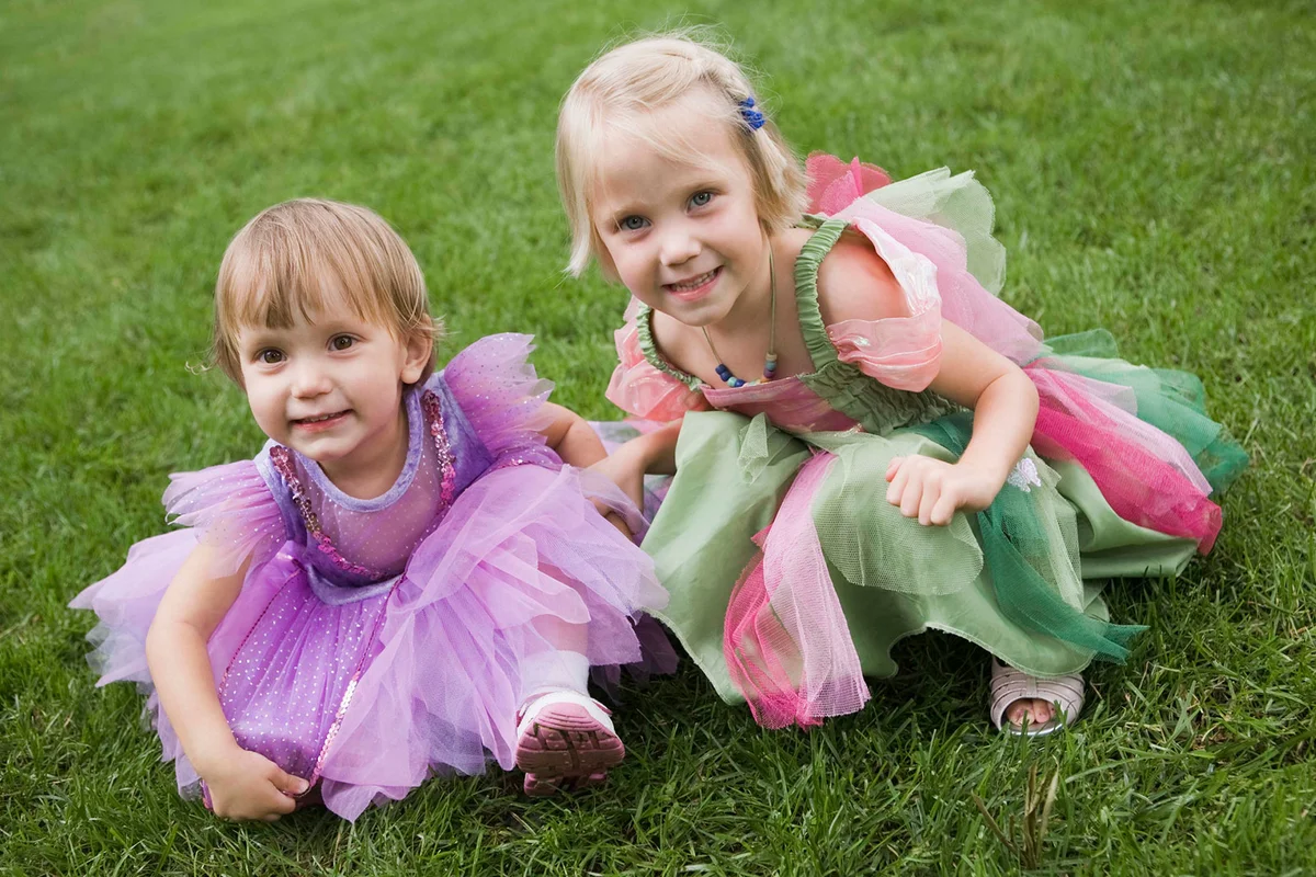 toddler girls in fairy costumes sitting on grass outside