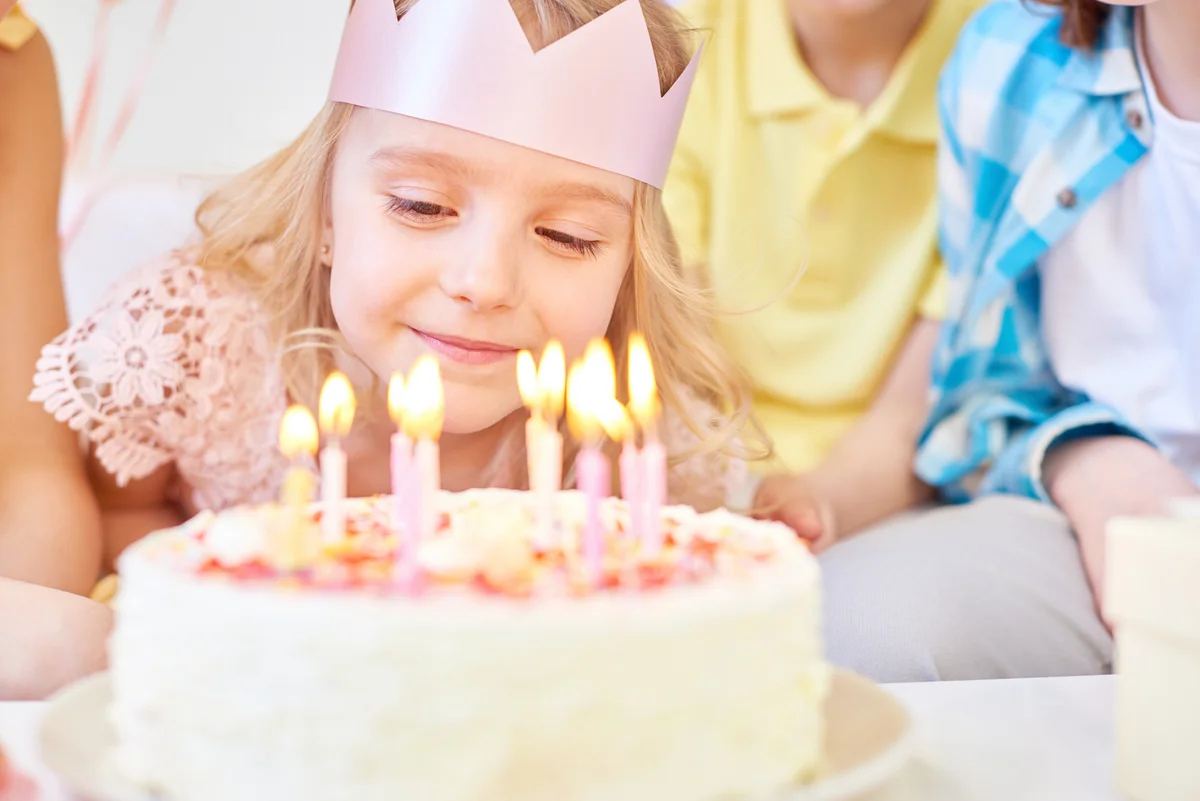 girl in crown blowing out birthday candles