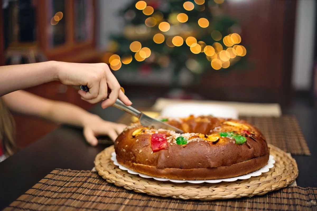Woman cutting epiphany cake besides the Christmas tree