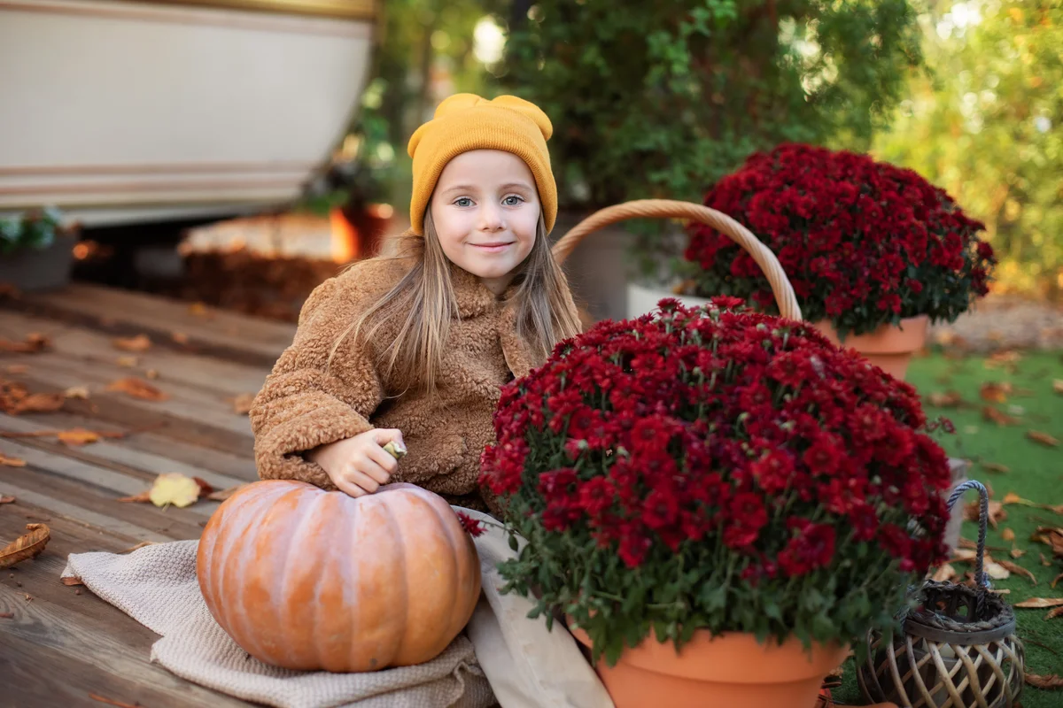 girl on porch with pumpkin and flower mums decoration in autumn