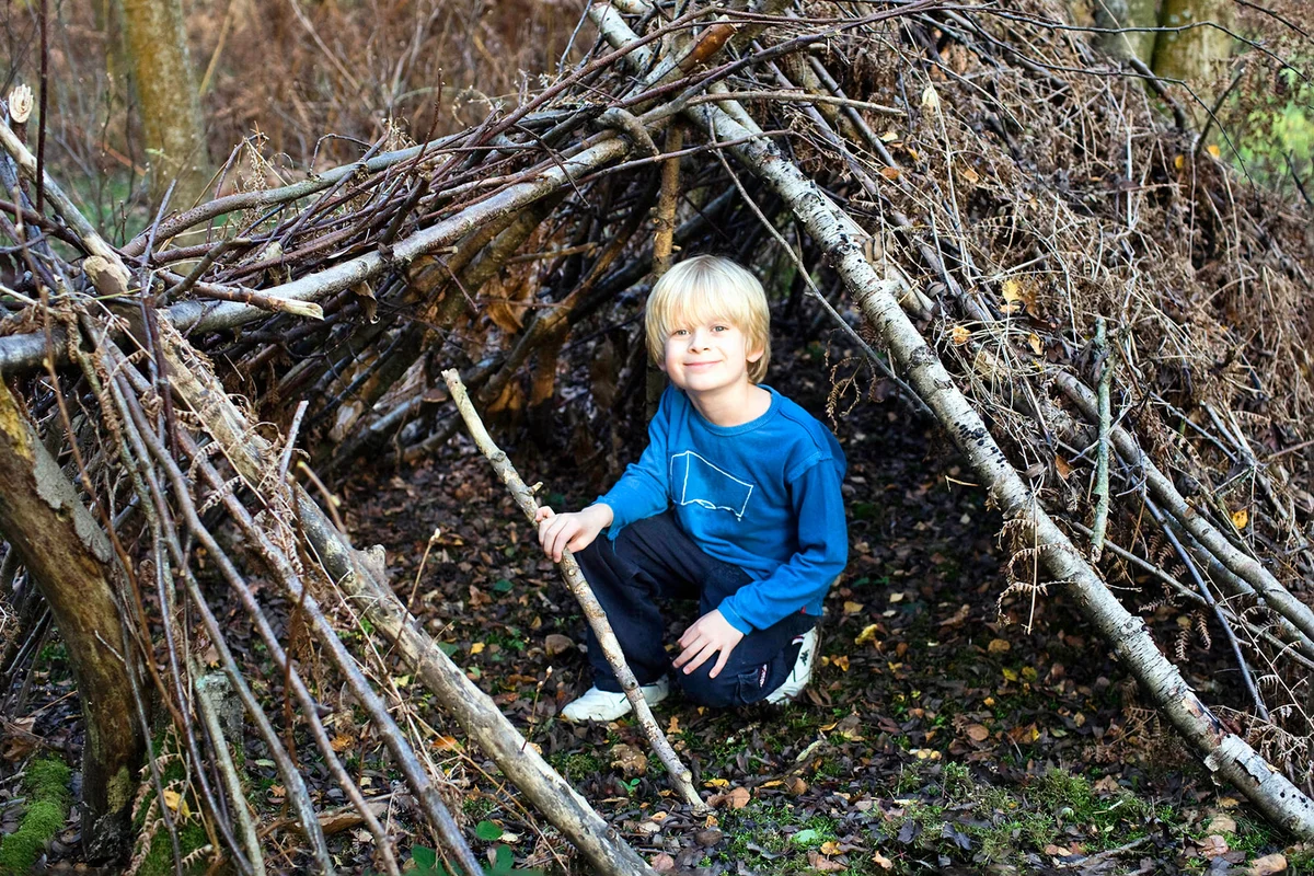boy in forest with fort den made of tree branches