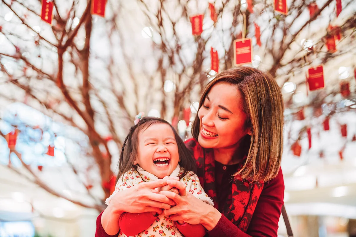 Pretty young mom making kung hei fat choy hand gesture with her lovely daughter joyfully in Chinese New Year