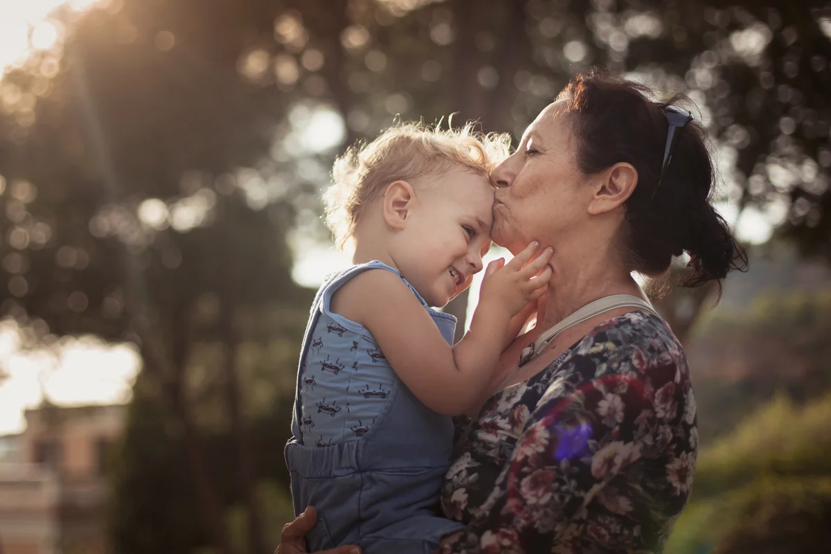 Toddler holding grandma's face while she kisses him